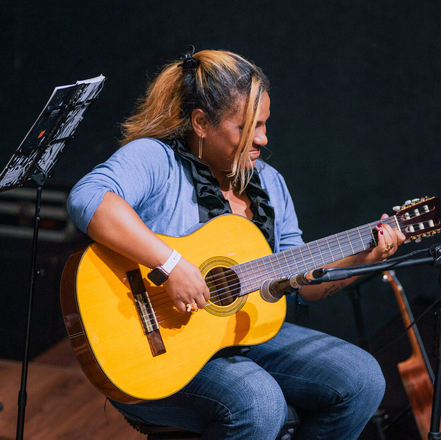 professora negra sentada tocando seu violao no recital melodica dezembro de 2023